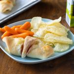 Ham and cheese rolled up in Rhodes dough. Roll up is on a plate with chips and carrots.