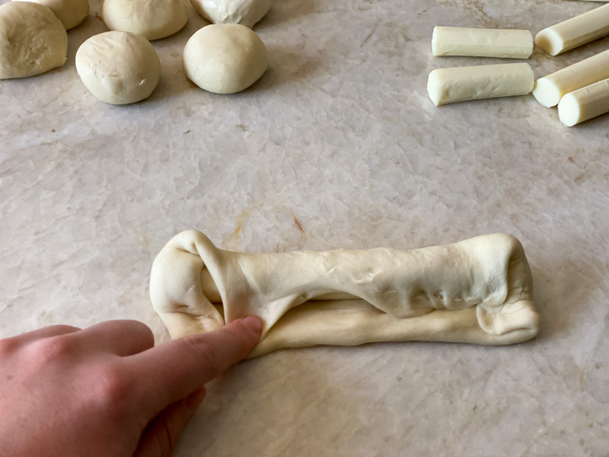 Dough being wrapped around cheese stick.