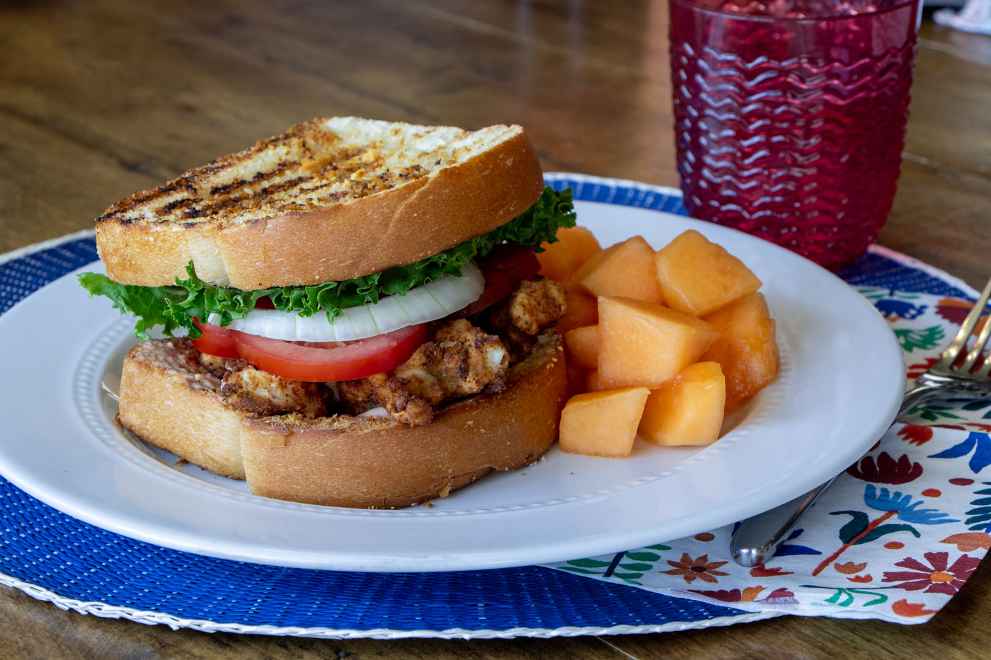 Fried chicken sandwich on a white plate and blue placemat.