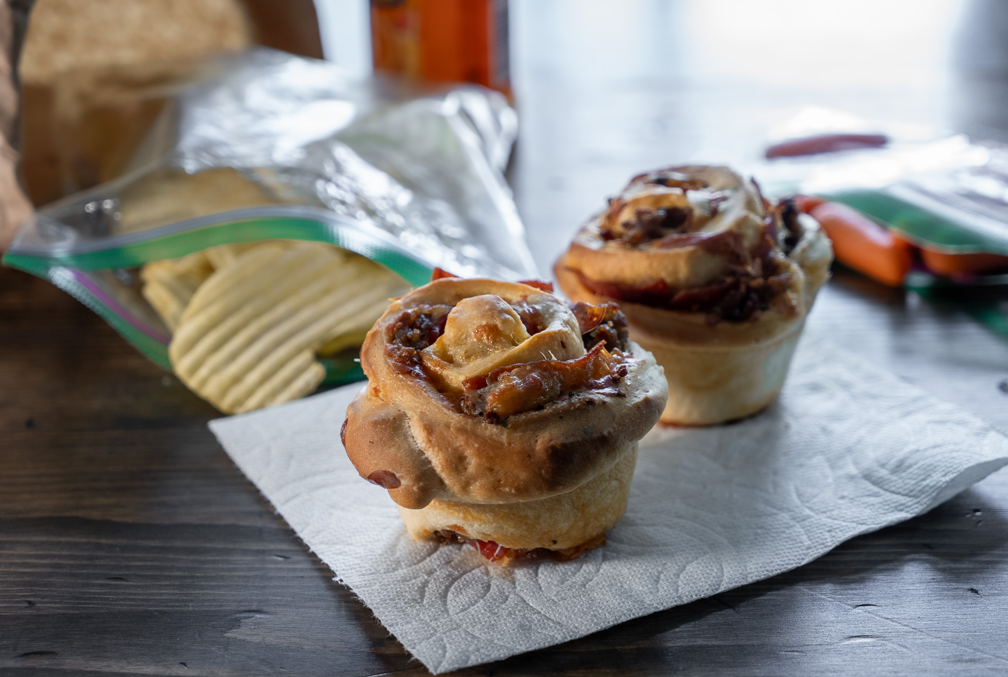 Pizza muffins served as a school lunch with chips and carrots; brown paper bag in the background.