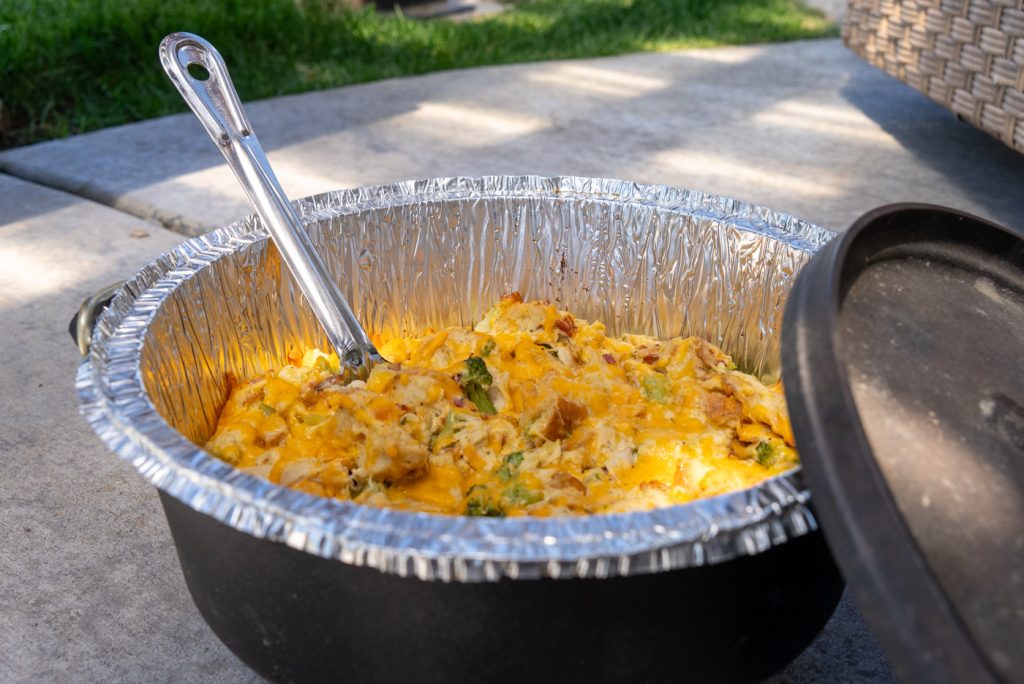A Dutch Oven dinner packed with broccoli, chicken and bacon and topped with cheese.